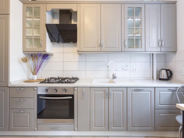 Grey raised-panel kitchen cabinets with glass uppers and a black range hood
