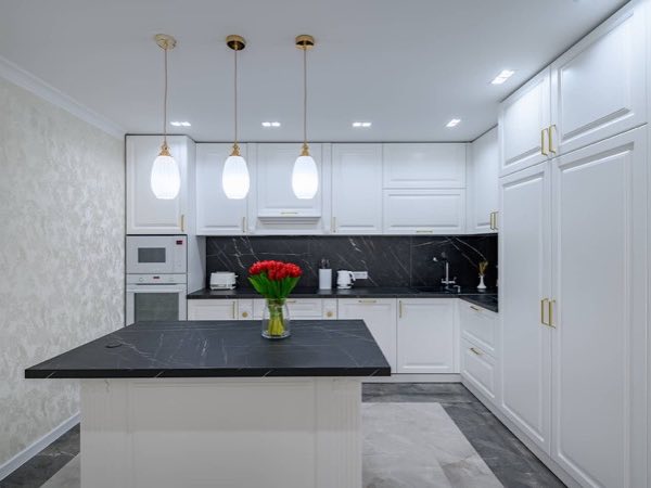 White kitchen with an island, a black countertop and glass pendant lights