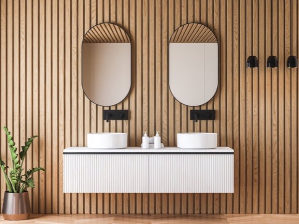 White double vanity with oval mirrors on a wood slat wall